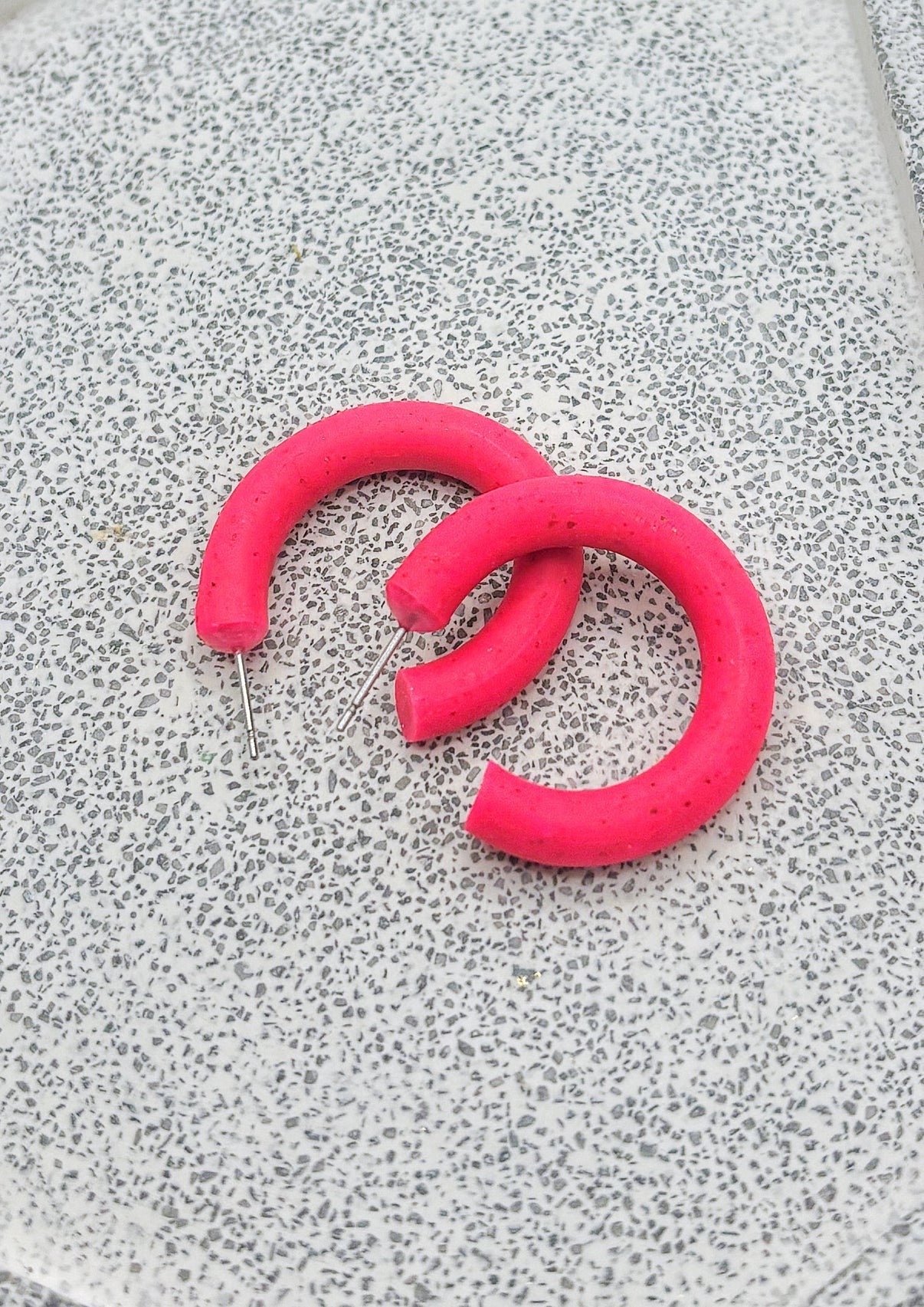 Paire d'anneaux rose fluo légèrement tachetés de noir presque entier. Ils sont déposés sur une dalle grise.