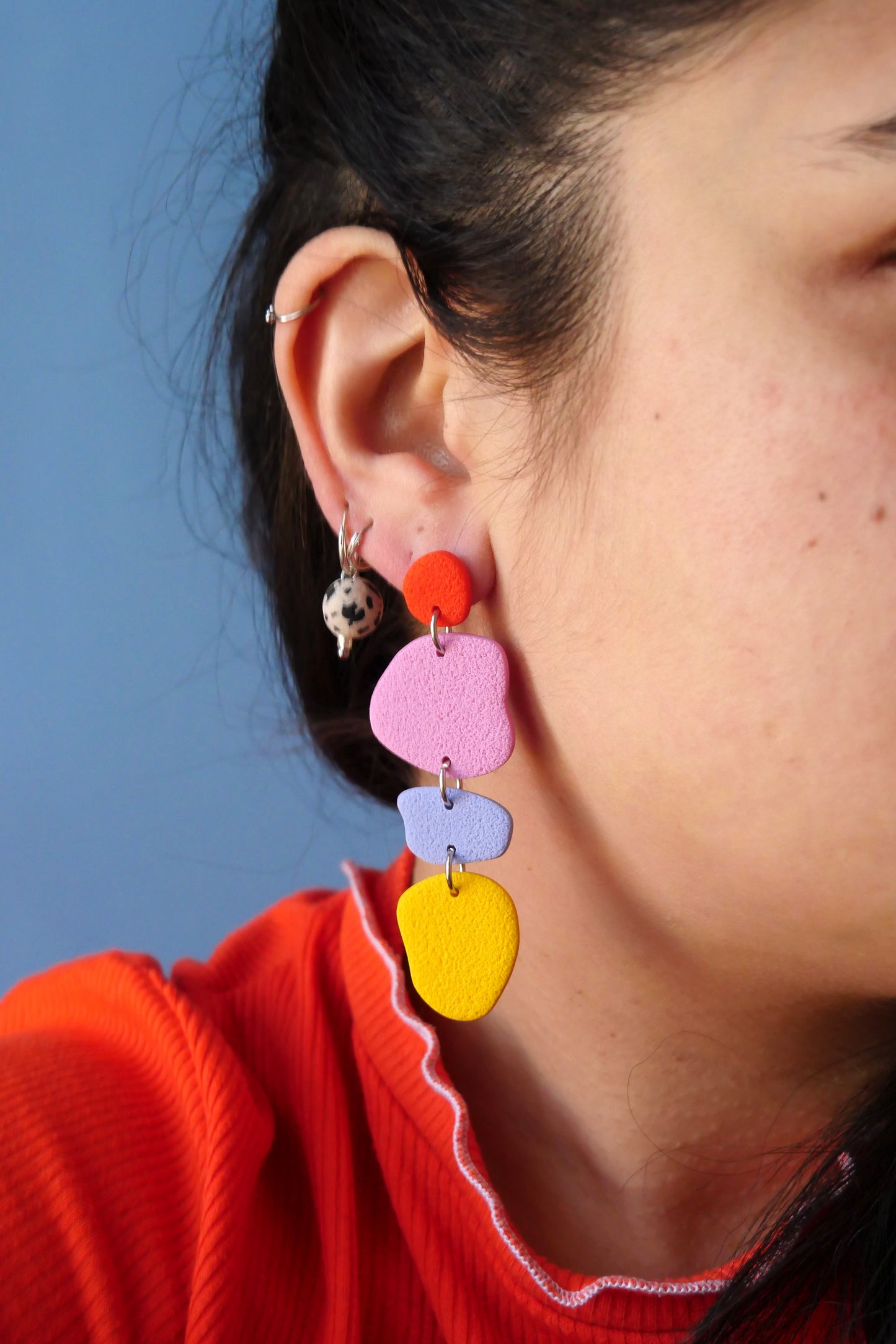 Paire de boucles artisanales multicolores en argile texturée, style artistique abstrait portée par une femme de profil