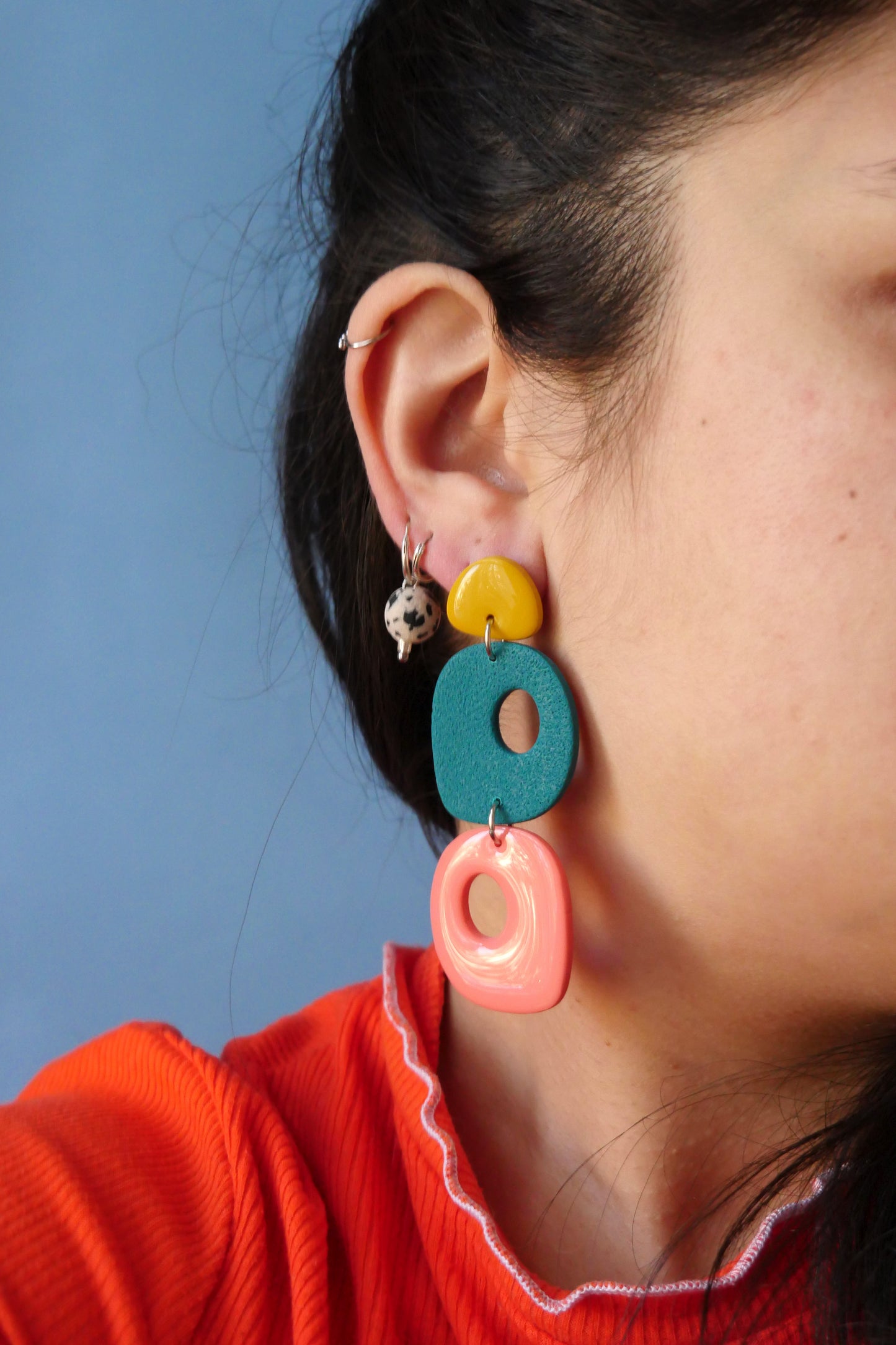 Femme portant une boucle d’oreille faite main en argile polymère, aux couleurs jaune, vert et rose, avec un design organique ajouré