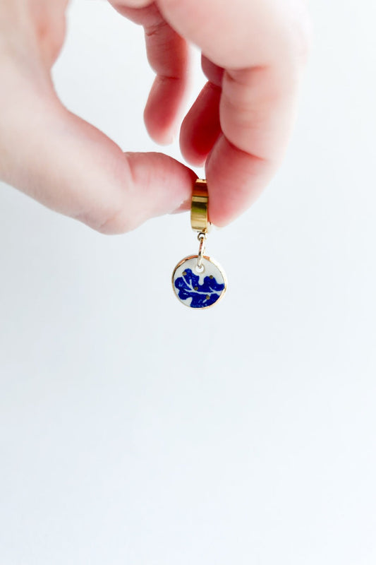 Gros plan d’une boucle d’oreille Always bleu en céramique et or 22k, tenue entre les doigts