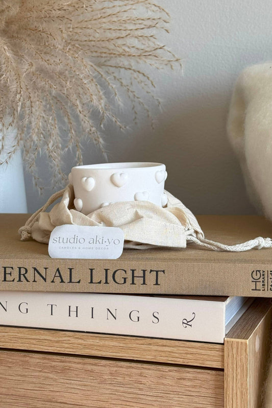 Bougie blanche à cœurs en relief présentée avec sa pochette en tissu naturel, ambiance cocooning.