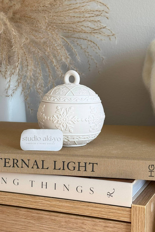 Bougie boule de Noël avec couvercle flocons, parfum frais et boisé, décoration hivernale chic.