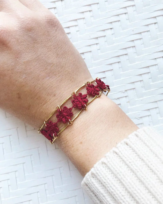 Bracelet Amalfi en chaîne dorée avec fleurs brodées rouges, porté au poignet sur fond clair