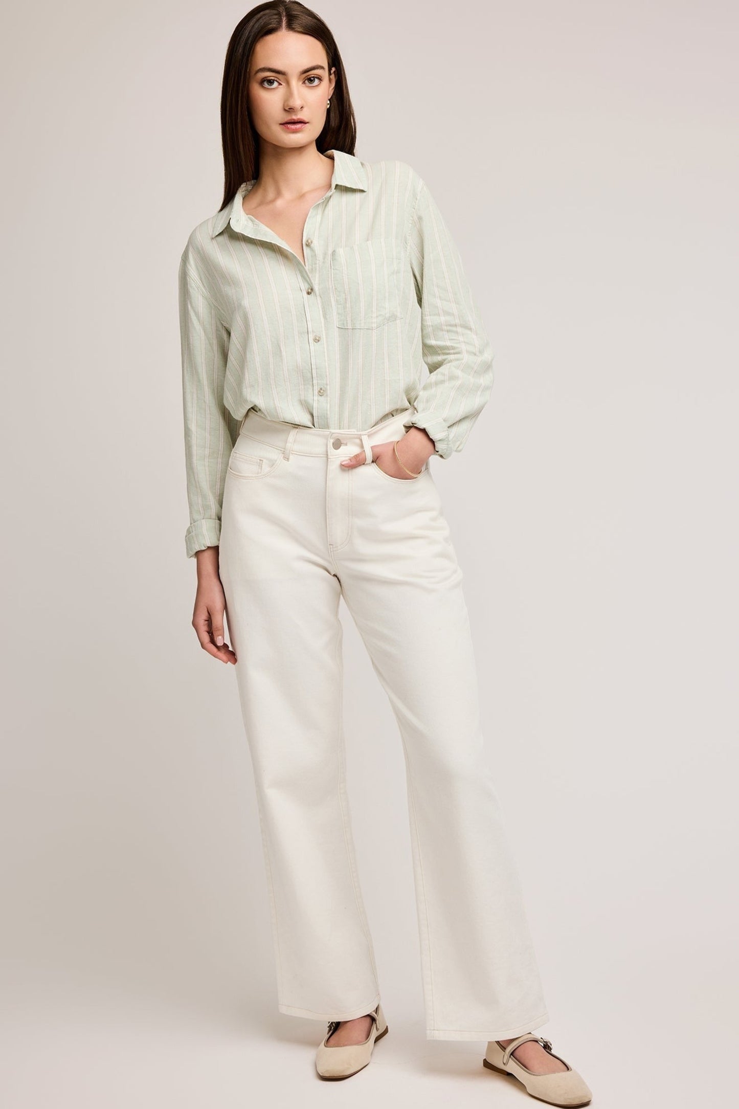 Chemise rayée vert sauge portée de face avec coupe fluide et boutons, portée avec un jeans blanc
