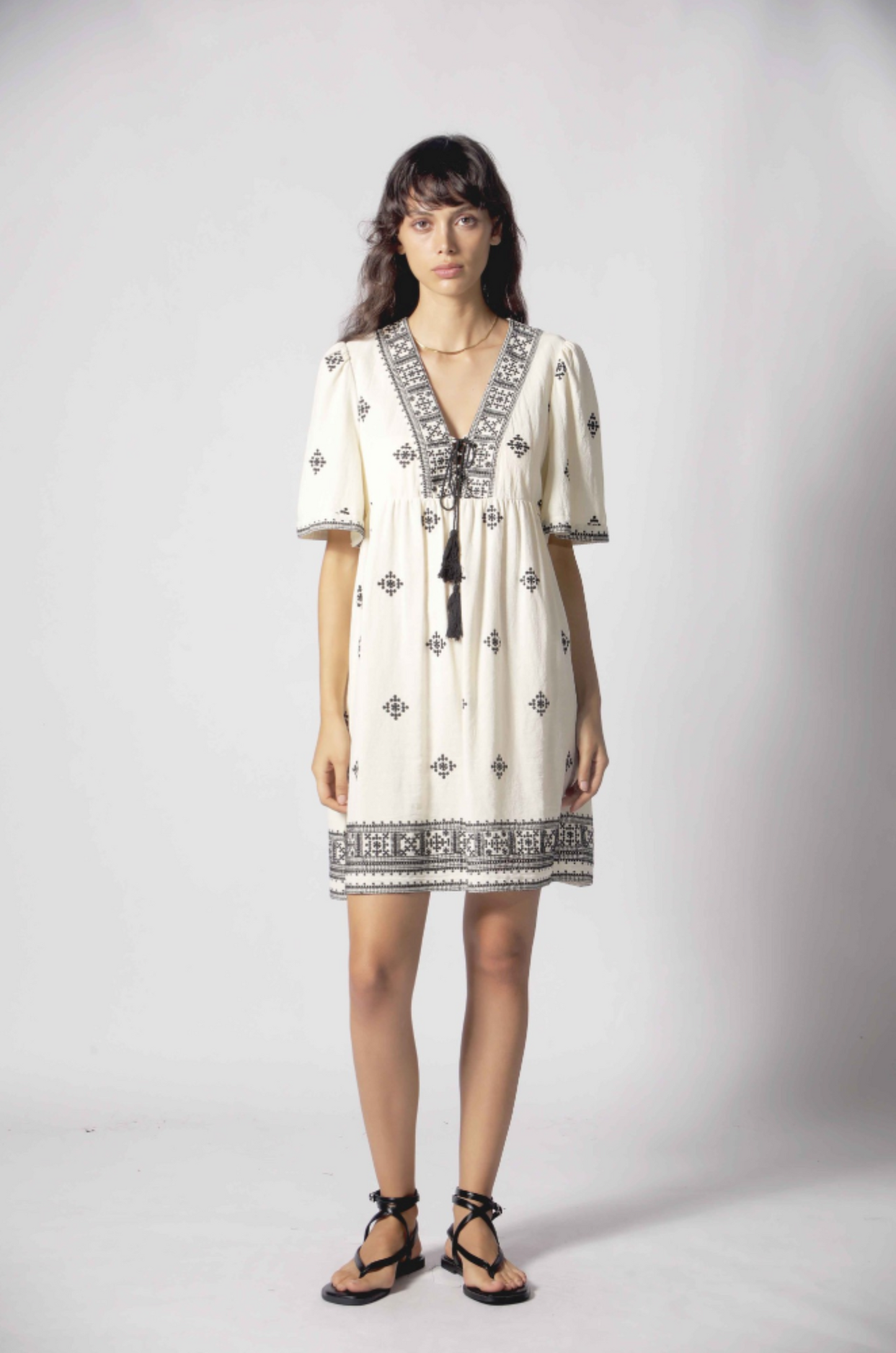 Robe Clelia blanc en coton avec broderies noires, bordure décorative et coupe courte estivale.