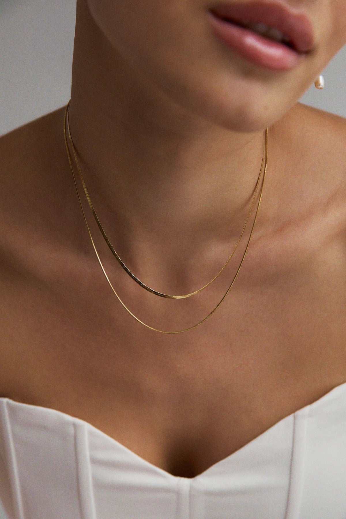 Collier Serenade or porté sur bustier blanc – deux chaînes serpent plaquées or, look raffiné