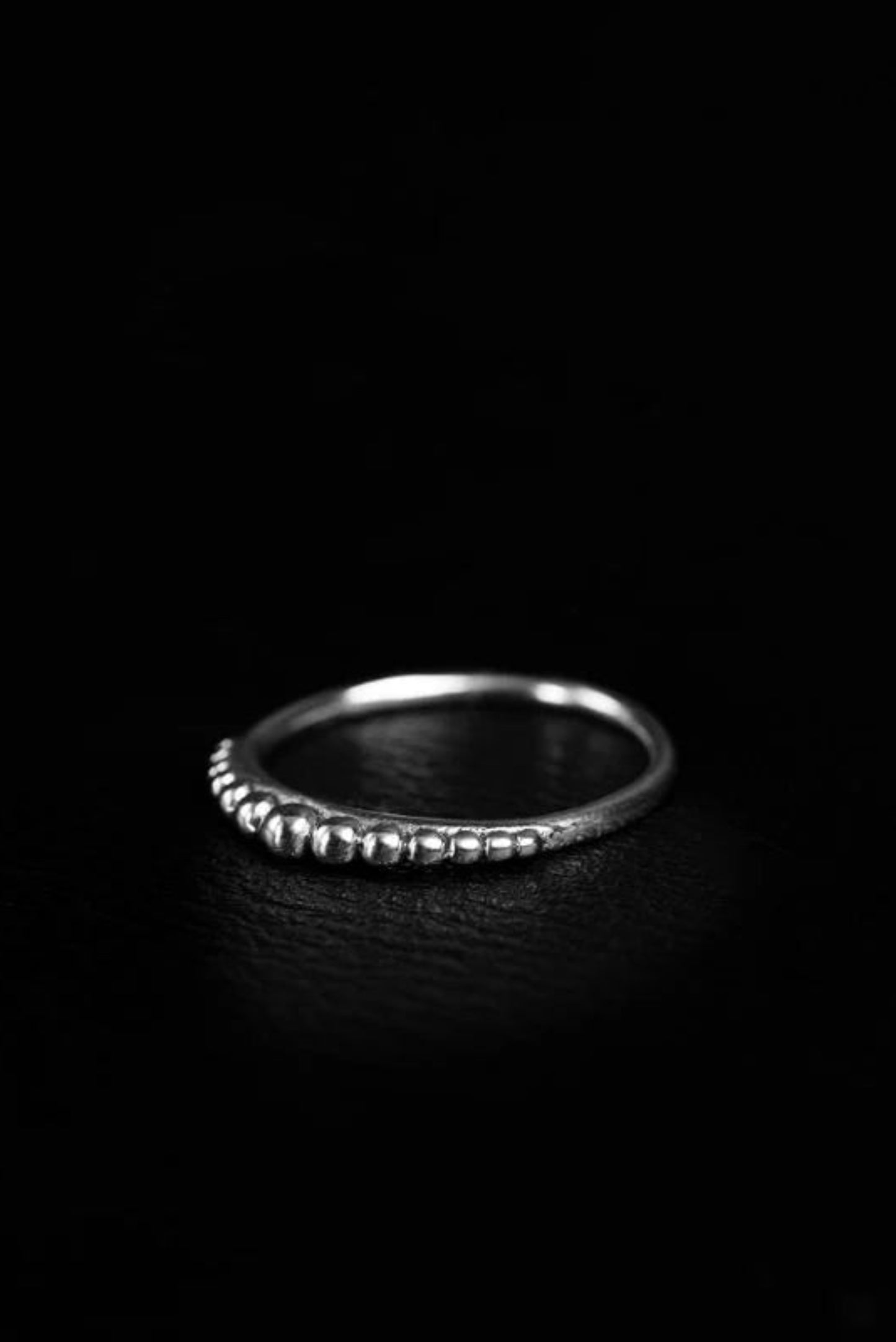 Bague Dots Argent posée sur fond noir, détail perlé discret et fini argenté lumineux.