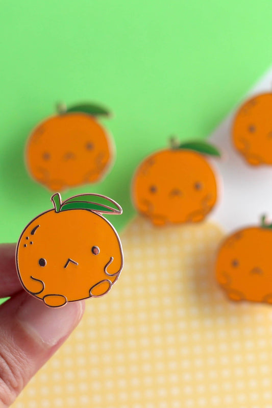 Ensemble de plusieurs épinglettes clémentine disposées sur un fond coloré.