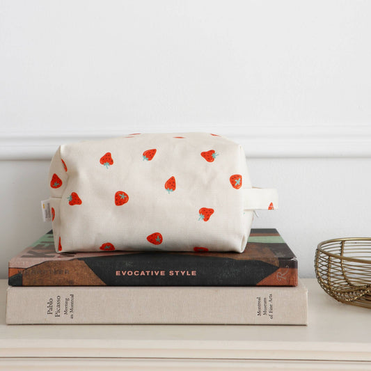 Grande trousse maquillage coton fraises posée sur des livres