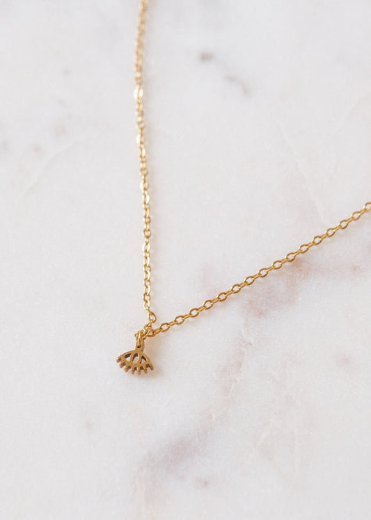 Fine chaîne dorée avec un pendentif en forme d’oeil. Le collier est déposé sur une pièce de marbre blanc.