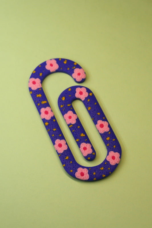 Marque-page trombone bleu posé à plat – fleurs roses et détails jaunes