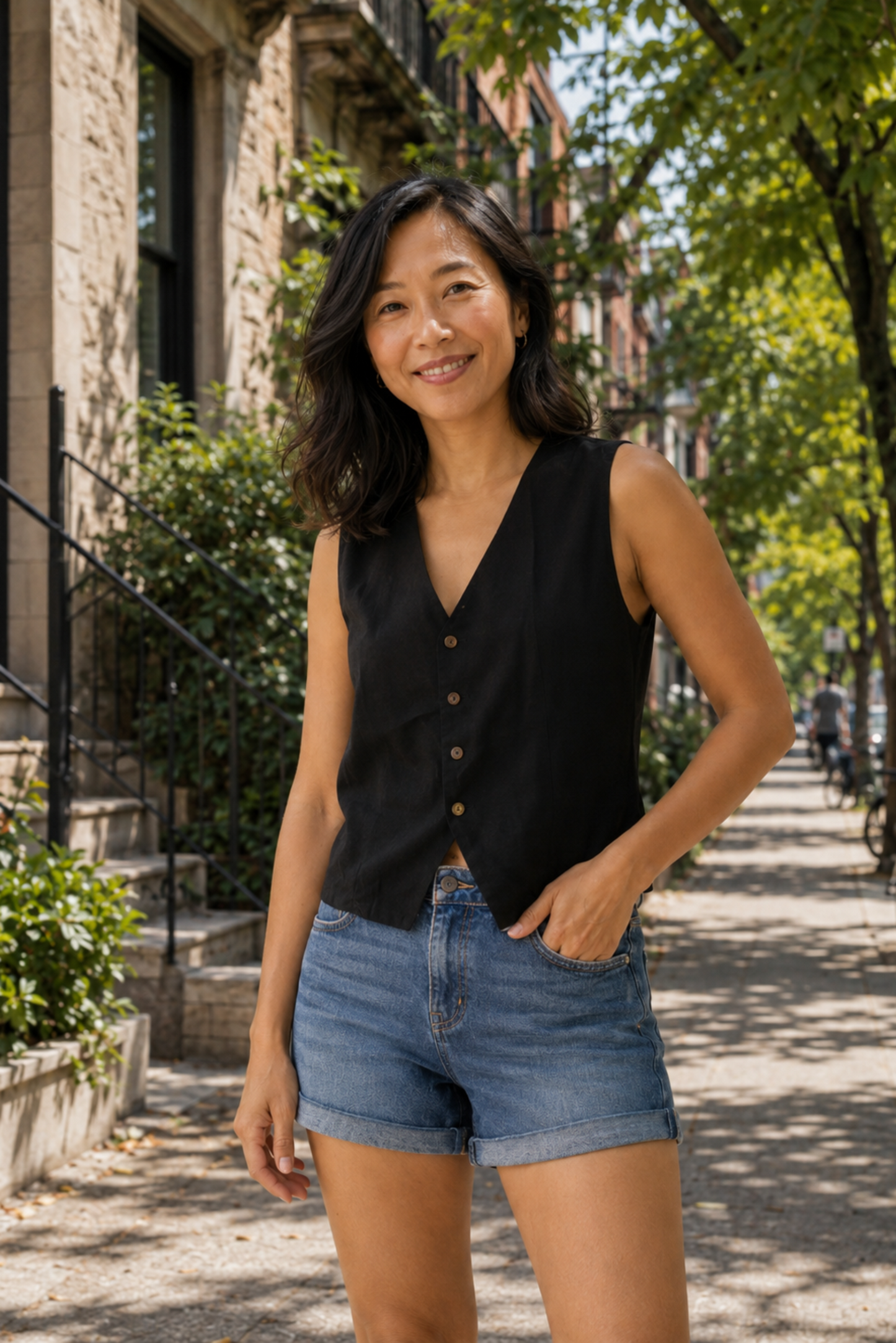 Femme portant la camisole Meli noir avec un short en denim, encolure en V, boutons devant et style chic décontracté.