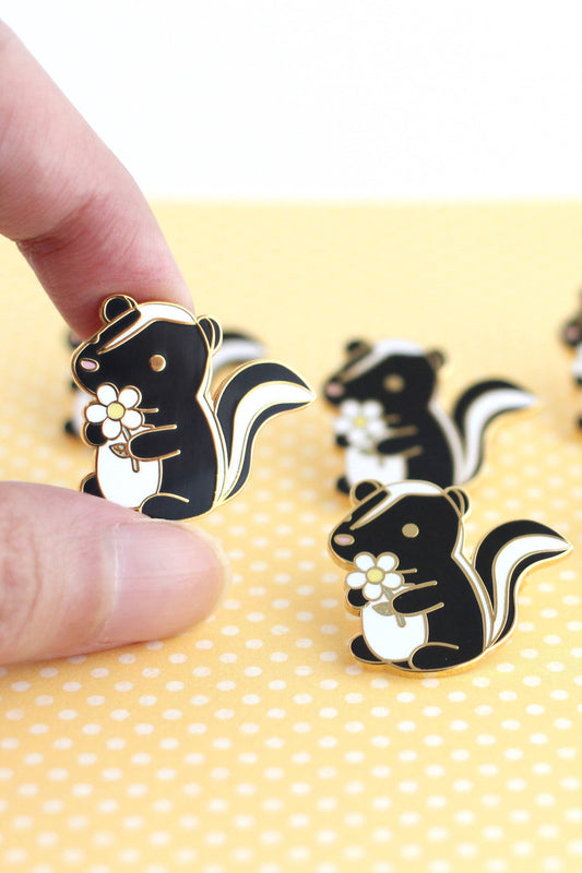 Épinglette mouffette fleur tenue entre les doigts – finition dorée