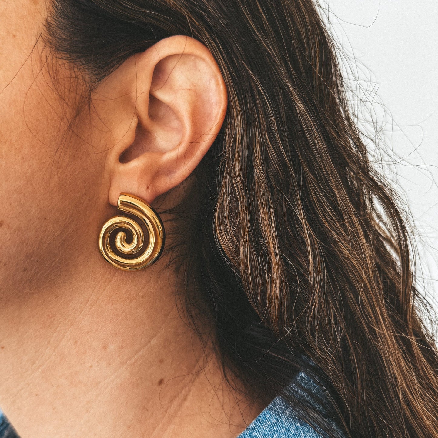 Boucles d'oreilles argent en acier inoxydable en forme de spirale portées par un modèle.