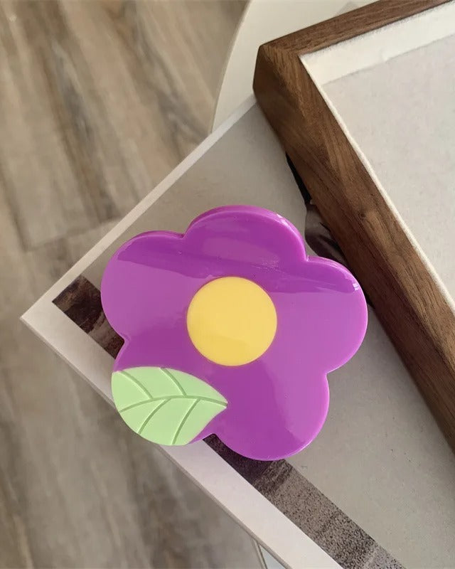 Pince à cheveux en acétate 6 x 7 cm en forme de fleur mauve avec centre jaune et feuille verte, vue de dessus