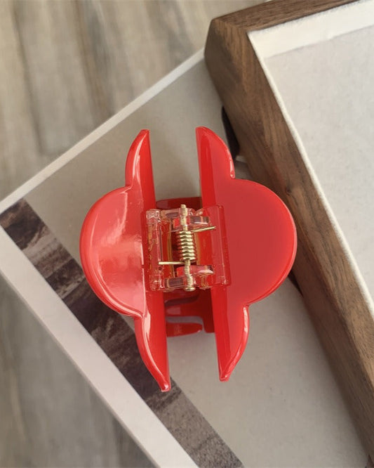 Pince à cheveux fleur en acétate rouge avec centre jaune et feuille verte, vue en angle