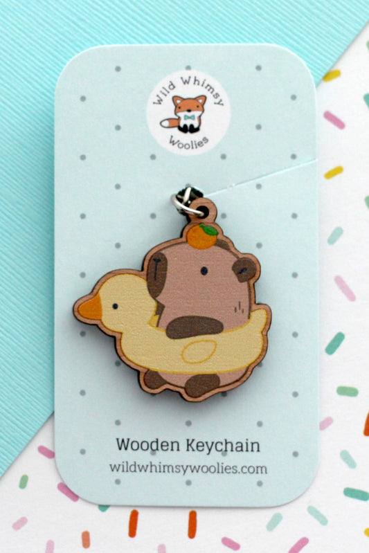 Porte-clés Capybara et Canard en bois de cerisier, présenté sur carte Wild Whimsy Woolies, fond à pois colorés.