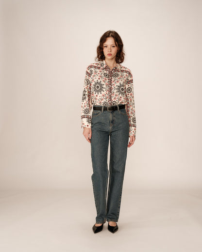 Une chemise fluide à manches longues ornée d’un imprimé bohème dans les tons crème, noir et rose. Le tissu léger et fluide accompagne une coupe légèrement ample, offrant élégance et confort. La chemise est portée avec un jean brut, créant une silhouette décontractée mais sophistiquée.