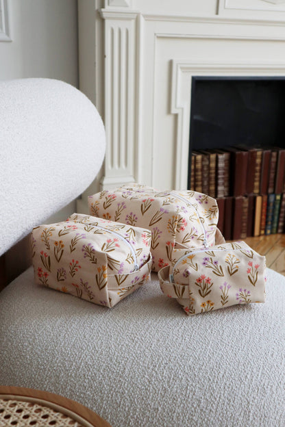 trio de trousses florales en coton beige posées sur un fauteuil