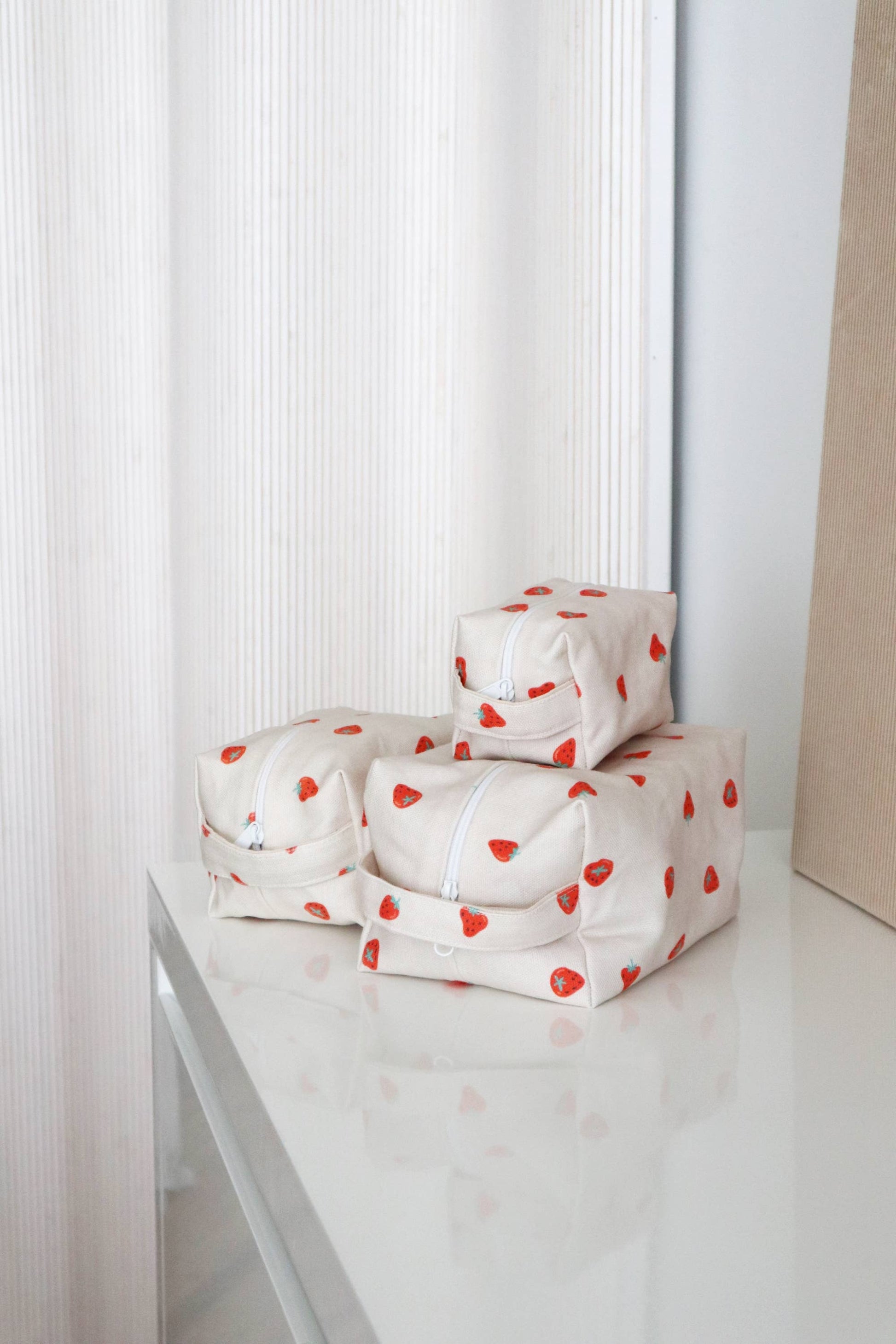 Trois trousses de maquillage en coton motif fraises, vues posées