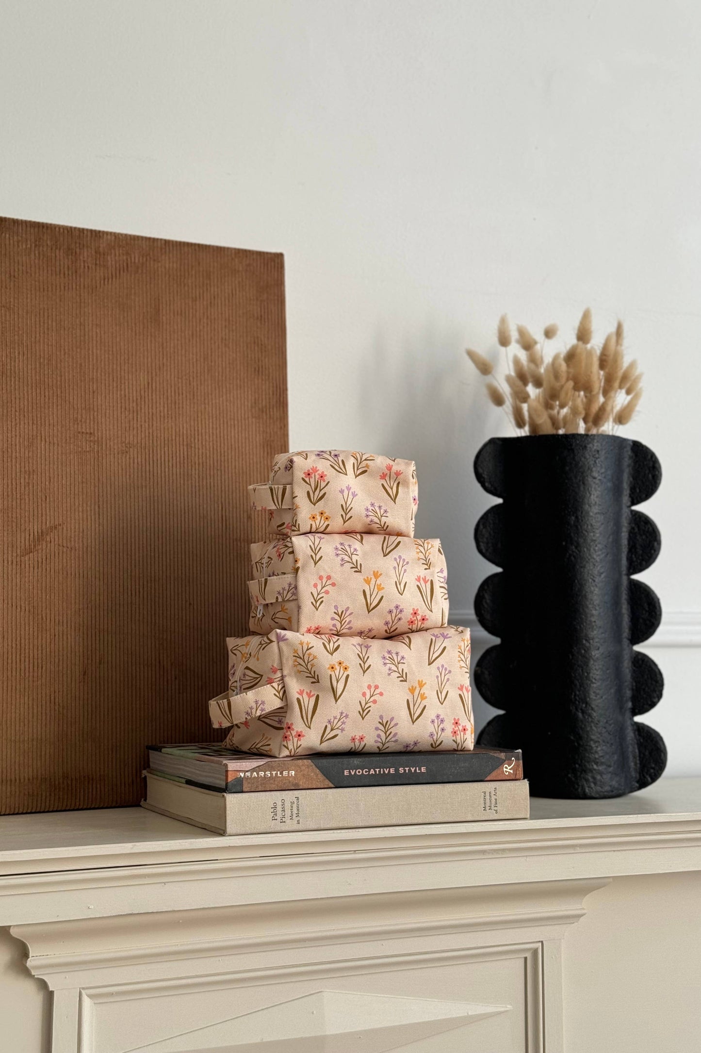 mini trousse florale en coton beige posée sur des livres dans un décor neutre