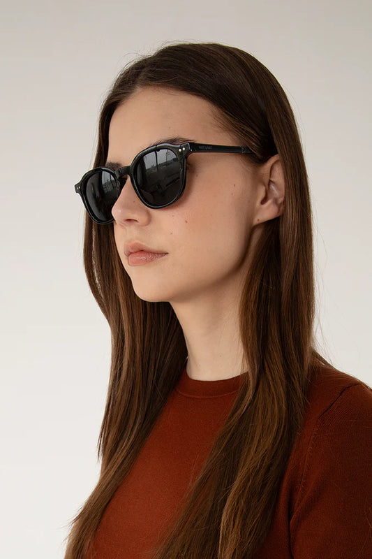 Femme portant les lunettes Nika noir en intérieur. Accessoire de voyage au style intemporel.