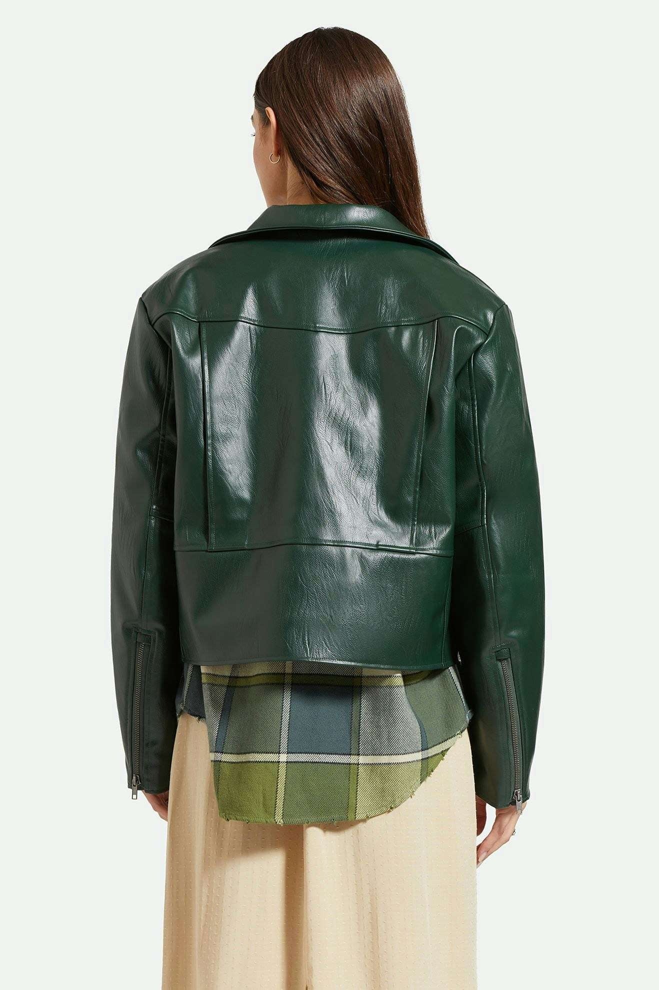 Manteau type perfecto en simili cuir lisse vert forêt porté par une femme. Le manteau est superposé sur une chemise et une robe longue. Vu de dos.