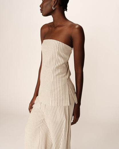 Top bustier beige à fines rayures verticales. Coupe ajustée avec un dos élastiqué pour un bon maintien. Fermeture latérale zippée et fente discrète sur le côté gauche. Confectionné dans un tissu fluide en fibres naturelles avec une doublure intégrée.