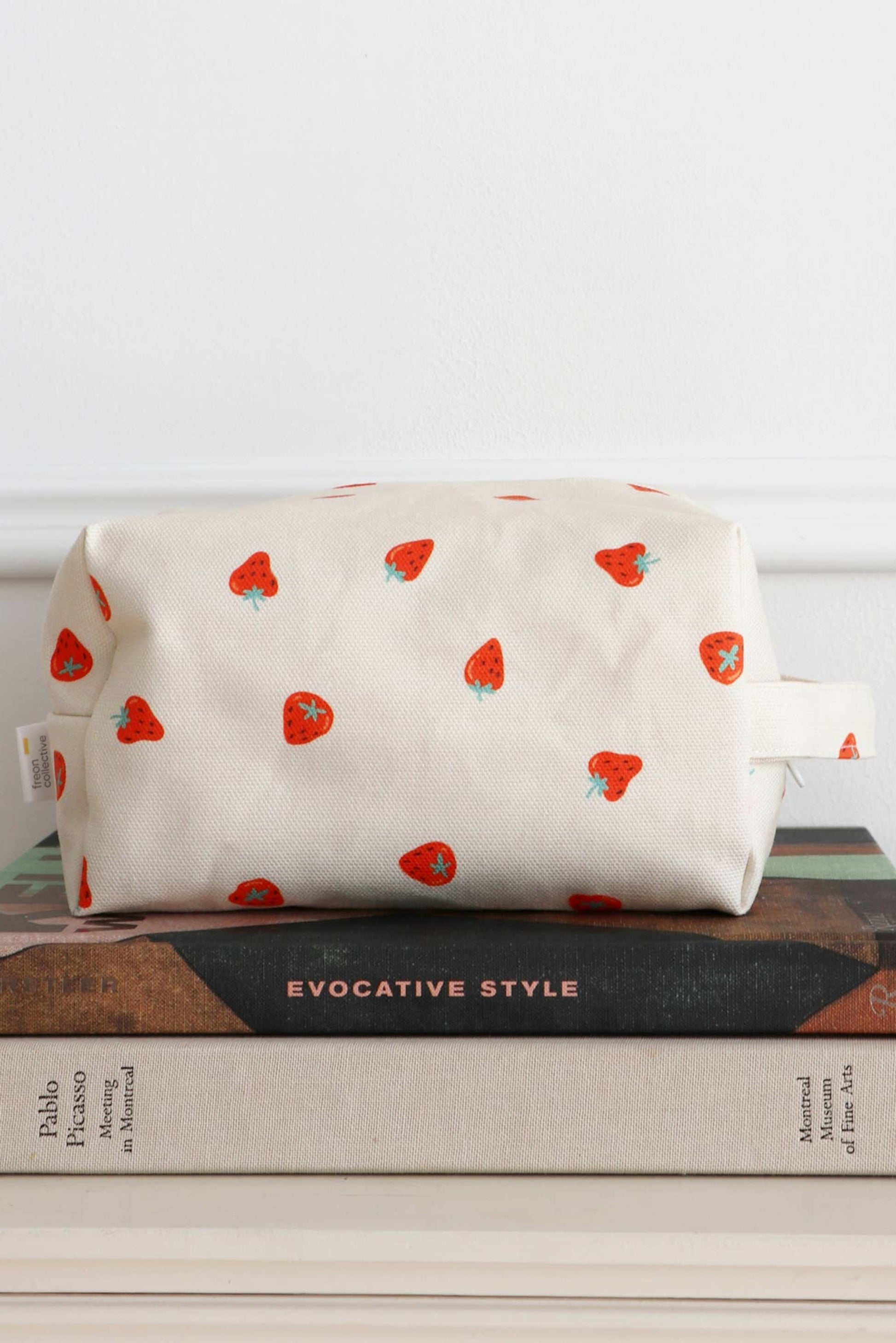 Petite trousse maquillage coton fraises posée sur des livres