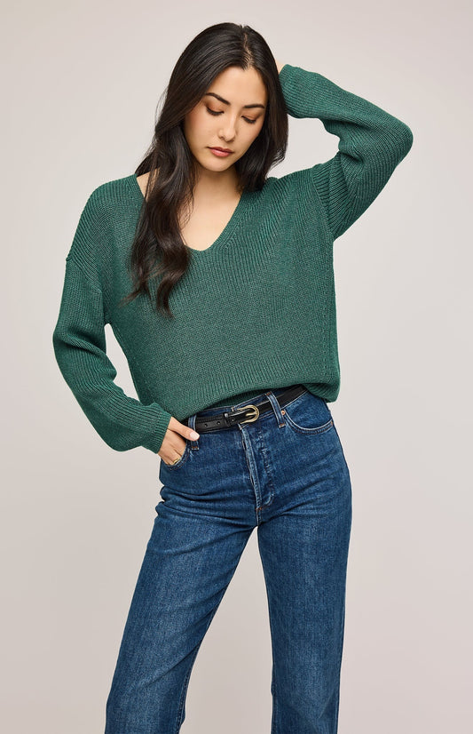 Femme qui porte un pull tricoté vert forêt avec un col en V associé avec un pantalon jeans indigo et un ceinture en cuir noir à boucle doré. Vu de face