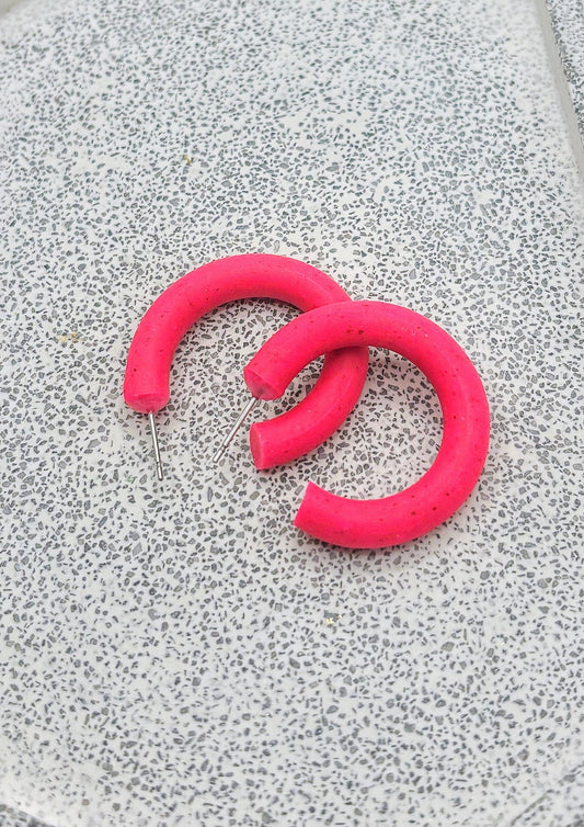 Paire d'anneaux rose fluo légèrement tachetés de noir presque entier. Ils sont déposés sur une dalle grise. 