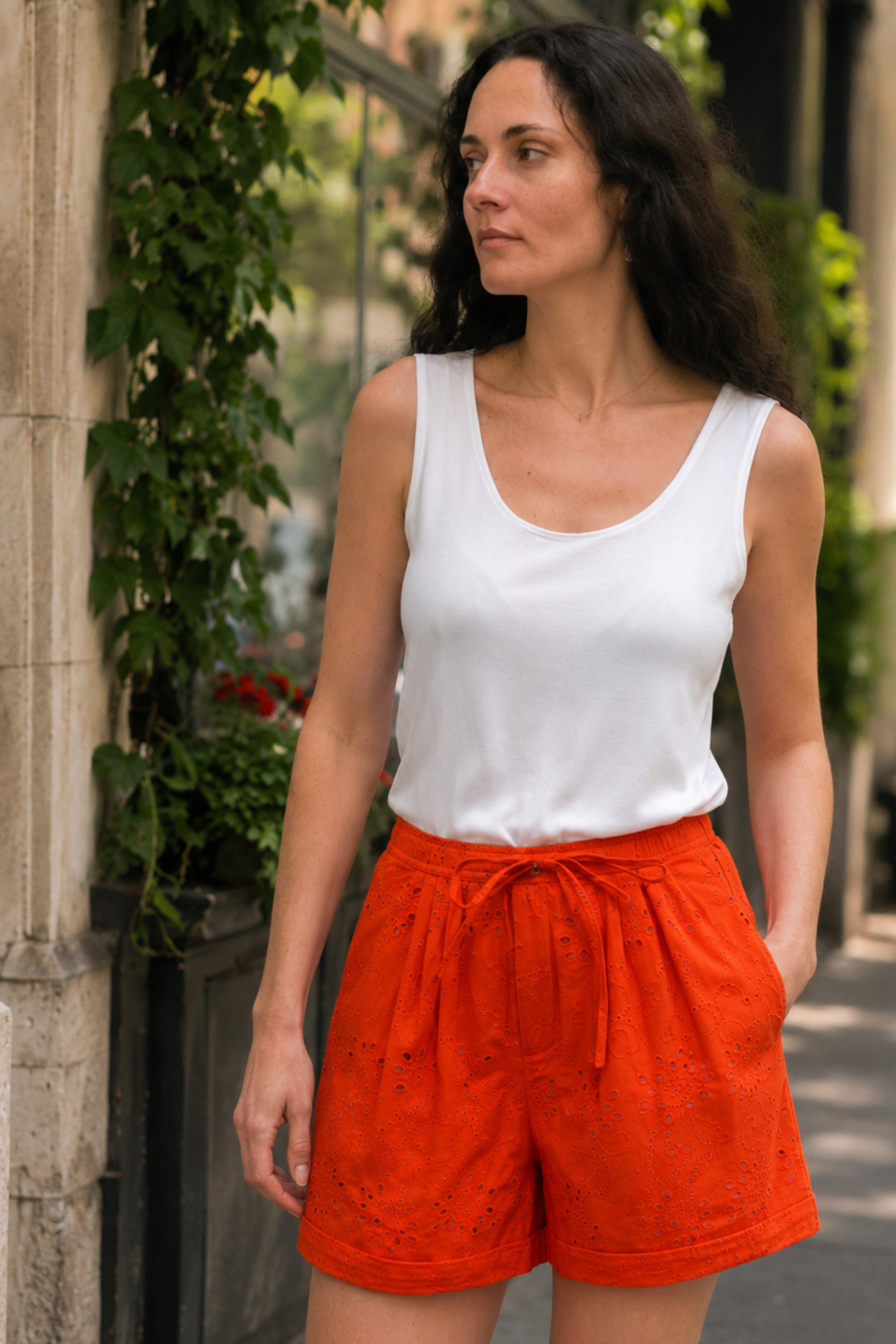 Femme portant le short Asha orange en broderie anglaise avec un débardeur blanc, taille élastique et cordon ajustable.
