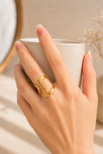 Bague Anna or portée sur la main tenant une tasse, avec lignes ondulées modernes et fini doré lumineux.