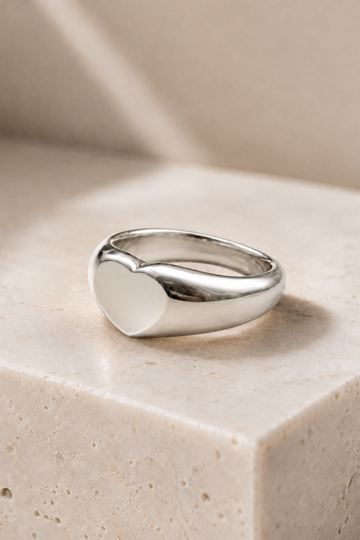 Bague cœur argentée posée sur un décor beige, fini poli brillant et forme bombée.
