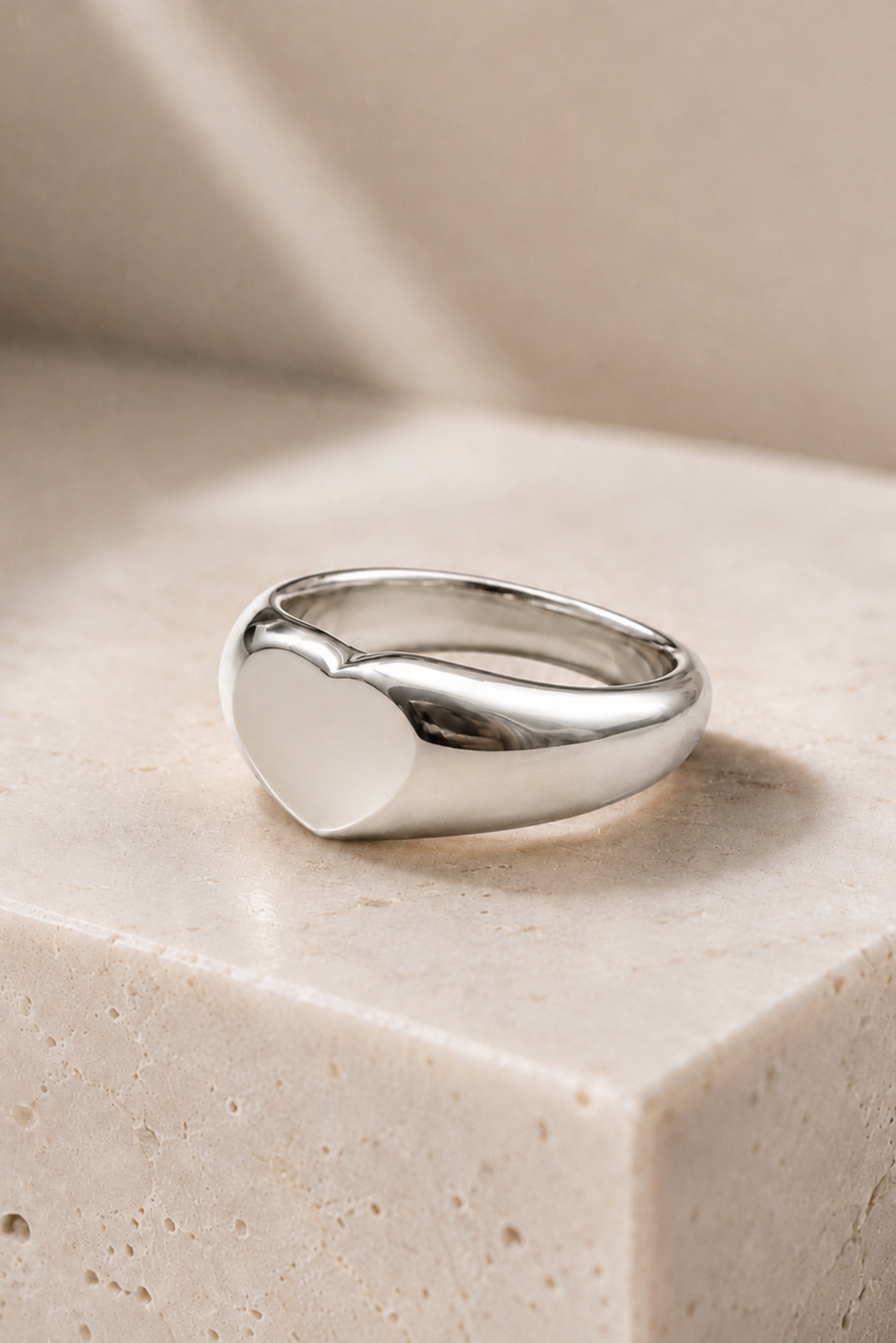 Bague cœur argentée posée sur un décor beige, fini poli brillant et forme bombée.