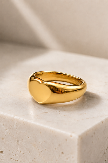 Bague cœur dorée posée sur une surface effet pierre, acier inoxydable plaqué or au fini brillant.