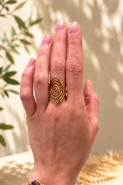 Bague spirale dorée portée à la main dans un décor estival élégant