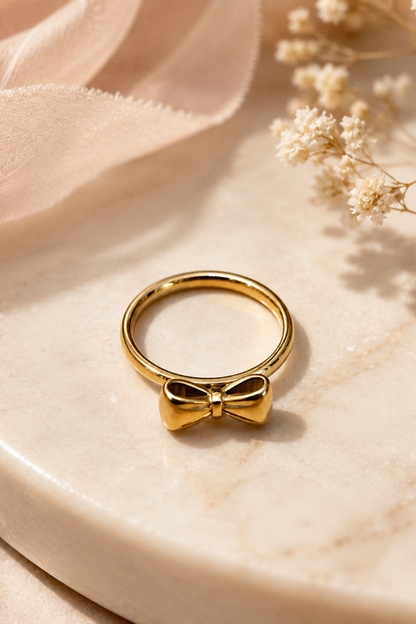Gros plan de la bague Ruban Nœud Or posée sur une surface beige, montrant son design en forme de nœud doré.