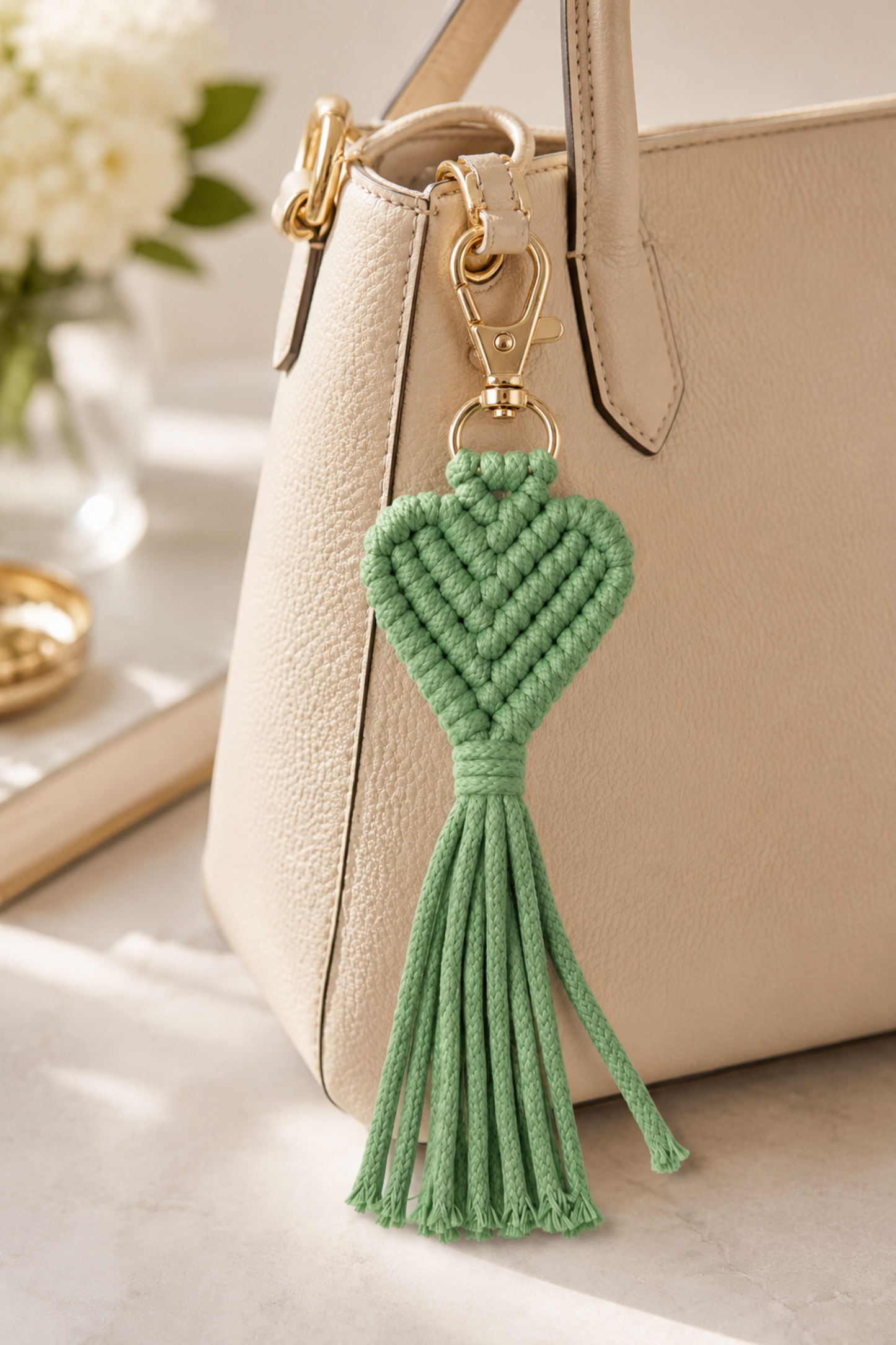 Porte-clé cœur en macramé vert accroché à un sac beige avec détails dorés.