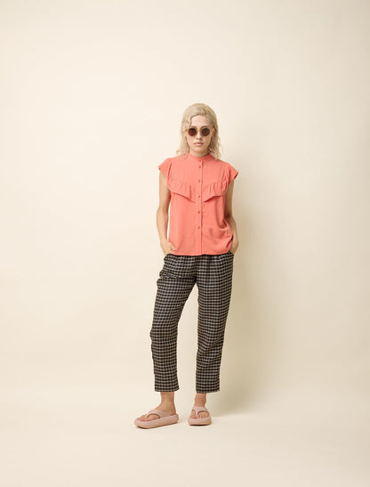 Blouse sans manches en coloris papaye. Ce haut fluide et léger présente un col montant boutonné et des volants délicats sur la poitrine, ajoutant une touche féminine et élégante. Sa coupe ample assure un confort optimal tout en apportant une allure décontractée et raffinée. Confectionnée dans une matière douce et respirante, elle est idéale pour les journées chaudes. Facile à assortir, elle se porte aussi bien avec un pantalon fluide qu'une jupe pour un style estival tendance et polyvalent.  