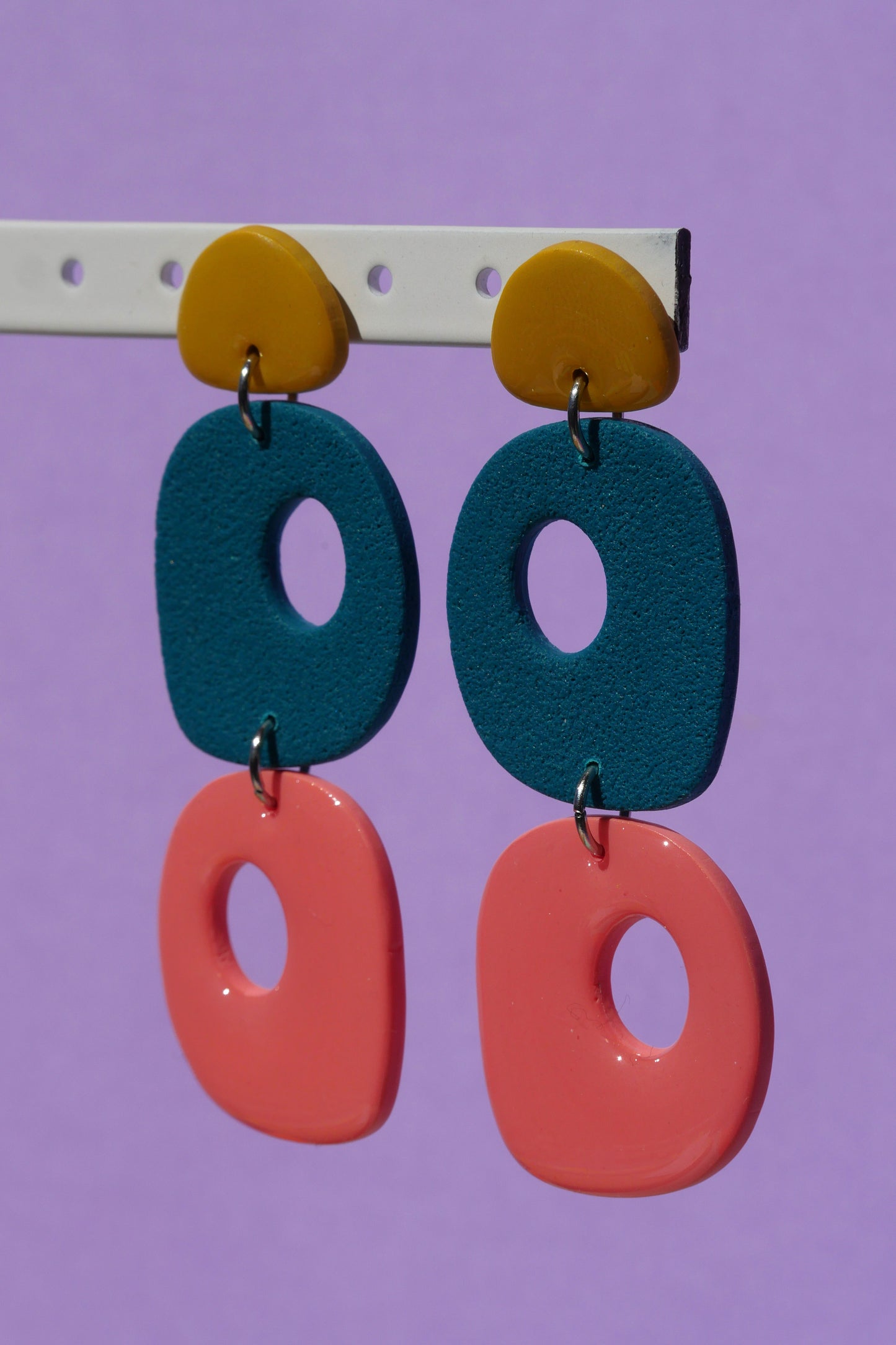 Boucles d’oreilles faites main suspendues, en argile polymère jaune, vert et rose, prises en photo sur fond violet en lumière naturelle

