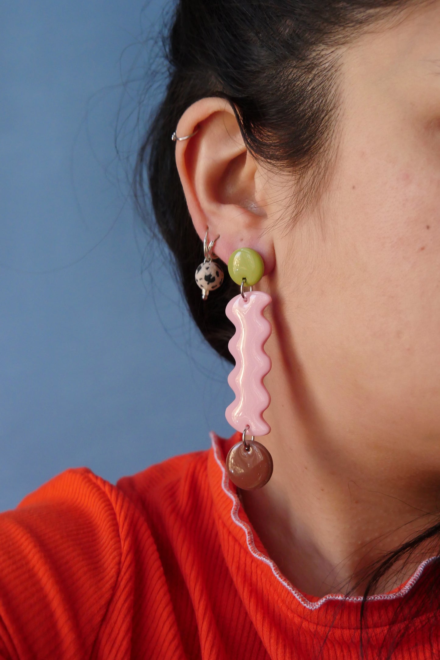 Paire de boucles d’oreilles en argile polymère multicolores avec forme ondulée – modèle fait main, portée par une femme de profil