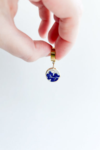 Gros plan d’une boucle d’oreille Always bleu en céramique et or 22k, tenue entre les doigts