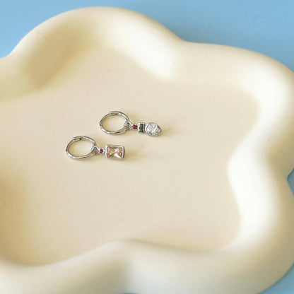 Vue des boucles d’oreilles créoles asymétriques posées sur un plateau crème