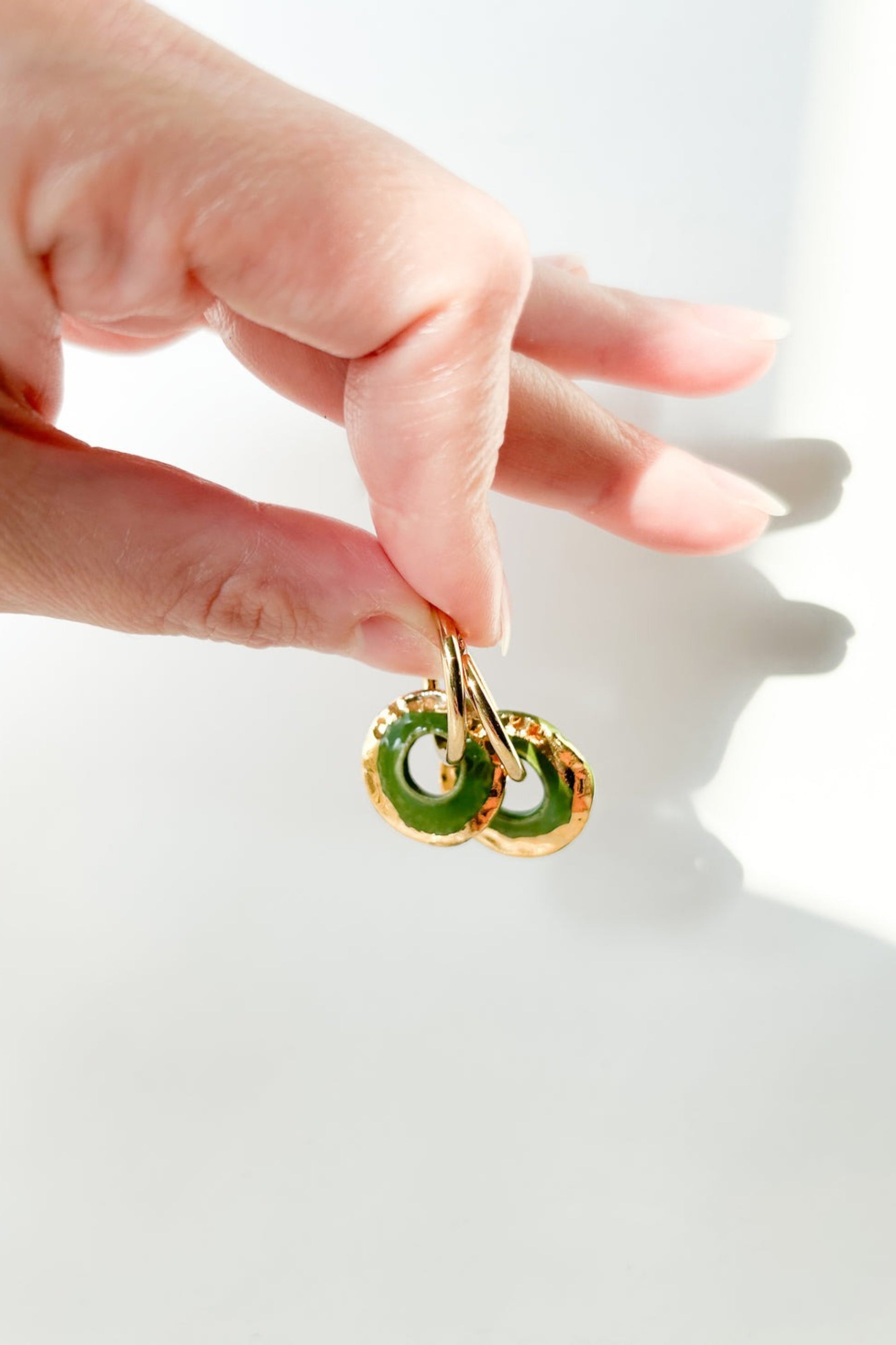 Gros plan des boucles d’oreilles Alegria vert en céramique et or 22k, tenues entre les doigts