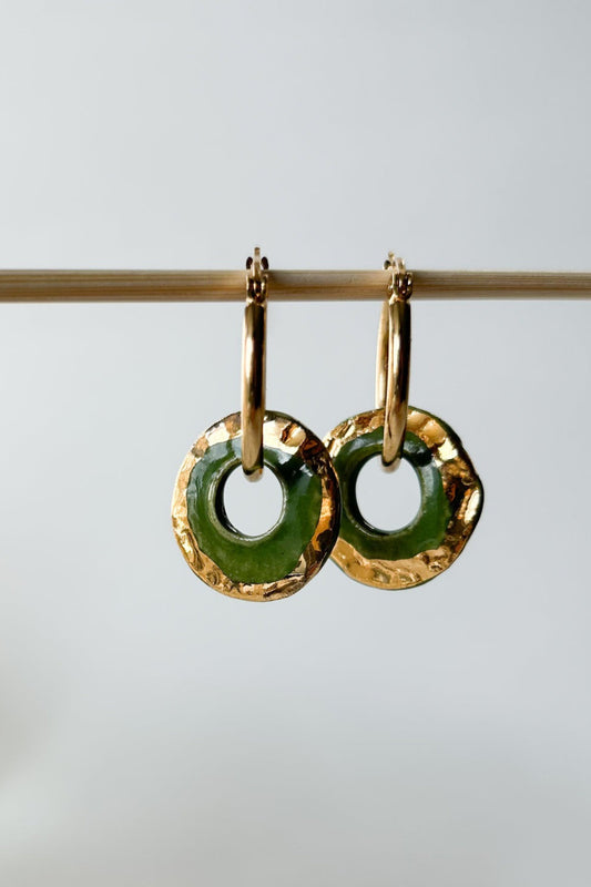 Boucles d’oreilles Alegria vert en céramique avec détails dorés, suspendues sur support en bois clair