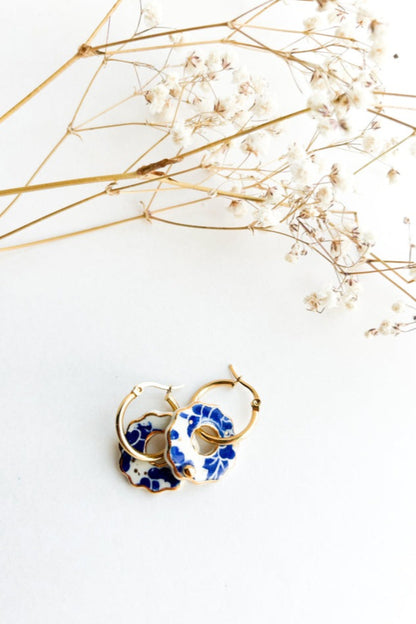 Boucles d’oreilles Donna bleu en céramique et or 22k posées sur fond blanc avec fleurs séchées décoratives