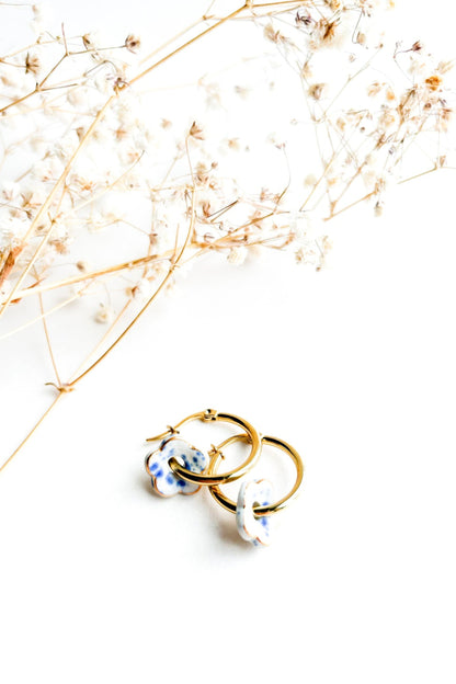 Boucles d’oreilles Poppy bleu en céramique et or 22k posées sur fond blanc avec fleurs séchées décoratives