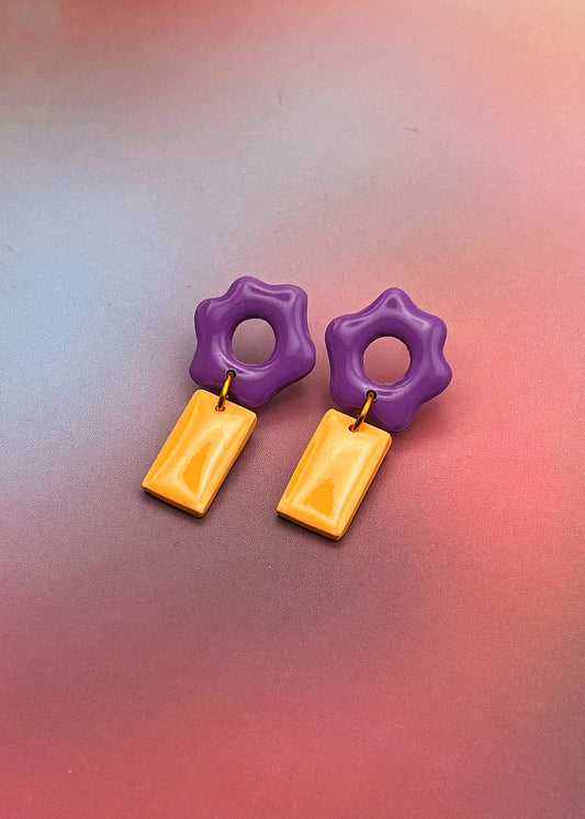 Boucles d’oreilles artisanales en argile polymère violet et orange, vue studio sur fond dégradé