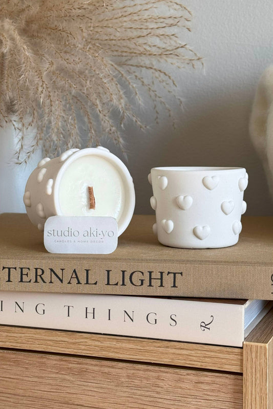 Bougie artisanale parfumée fraise et champagne, pot blanc à cœurs en relief, ambiance décorative douce.